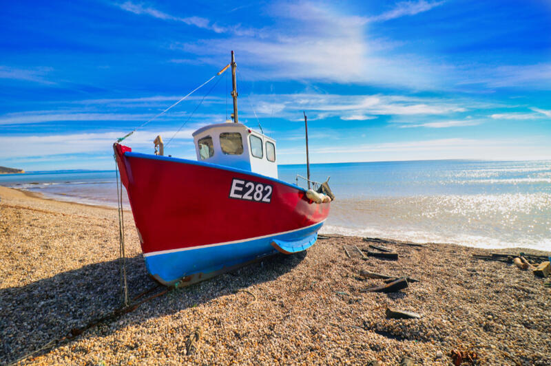 Fishing Boat on Beer Beach, Devon Red and blue fishing boat resting on the pebble beach at Beer in Devon, England, overlooking the sea beneath a bright blue sky.