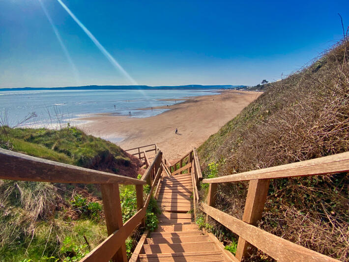 Wooden steps leading down to the sandy beach and sea at Exmouth in Devon, England, beneath a clear blue sky.